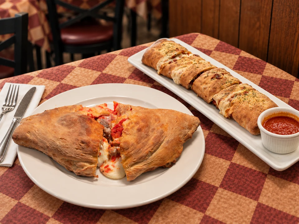 Calzone and Stromboli Roll together on Gumba’s checkered table. AI-assisted composite based on restaurant references.